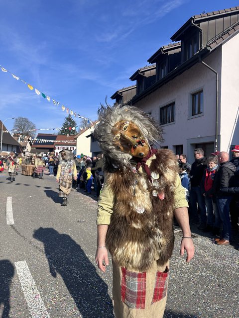Häx mit grauhaariger Maske, Fellweste und rotem Karorock auf der Strasse