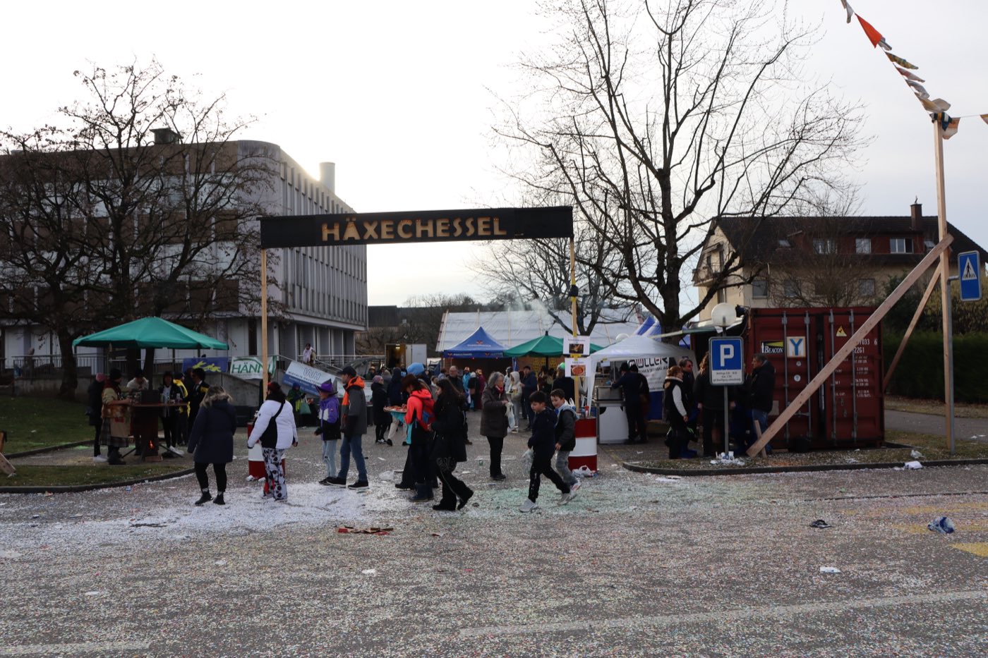 Festplatz Häxechessel mit hölzernem Torbogen, Zelten und Gästen auf konfettibedecktem Boden